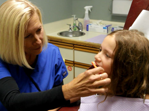 A dentist helping brush the teeth of a young girl sitting in a red dental chair at Alan B. Evans, DDS, PC in Muscatine, IA