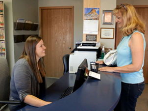 Receptionist at Alan B. Evans, DDS, PC sitting at a desk and speaking with a patient in Muscatine, IA