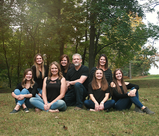 The entire dental staff of Alan B. Evans, DDS, PC wearing black over blue jeans sitting in a field under trees in Muscatine, IA