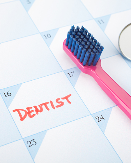 A calendar with Dentist written on the 16th and a pink toothbrush with blue bristles sitting on top