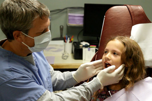 Dentist from Alan B. Evans, DDS, PC checking the mouth of a younger patient in Muscatine, IA