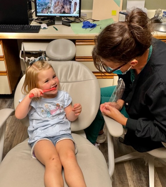 A dentist helping brush the teeth of a young girl sitting in a red dental chair at Alan B. Evans, DDS, PC in Muscatine, IA